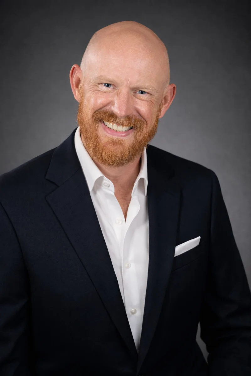 Rick Byrne smiling, wearing a dark jacket and white shirt
